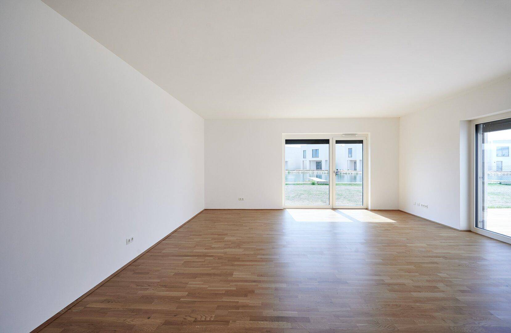 Heller, leerer Wohnraum mit Holzboden und Zugang zu einer Terrasse oder dem Garten.