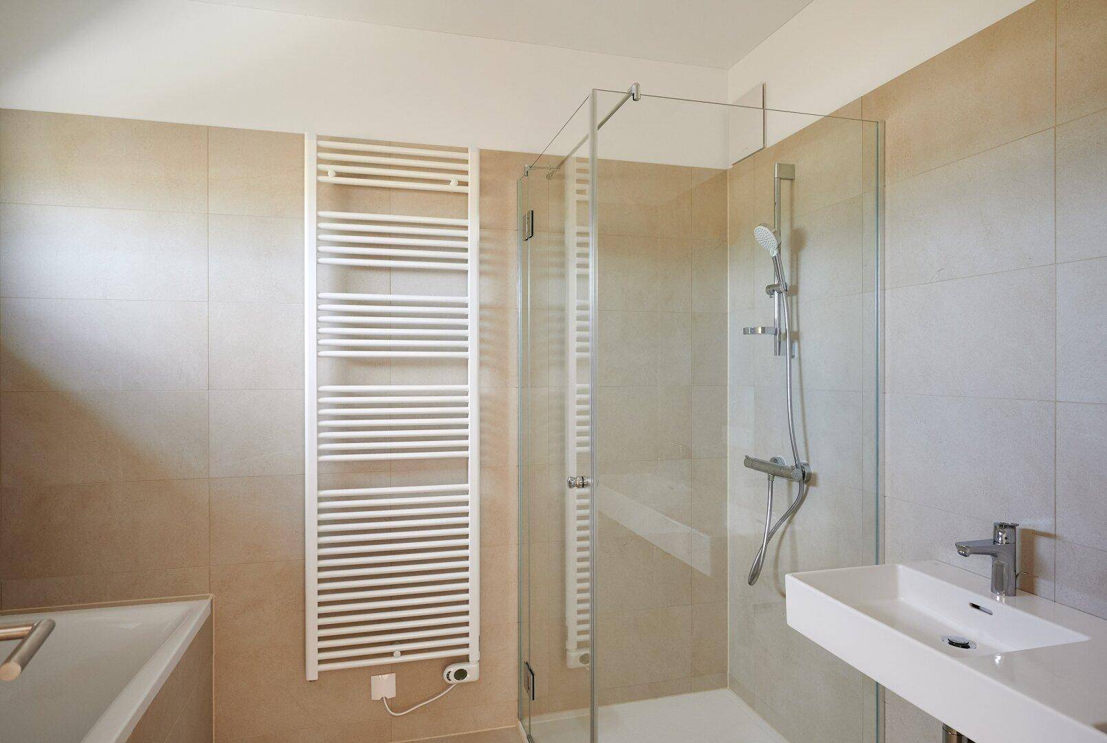 Modernes Badezimmer mit begehbarer Dusche, Handtuchheizkörper und beigefarbenen Fliesen.