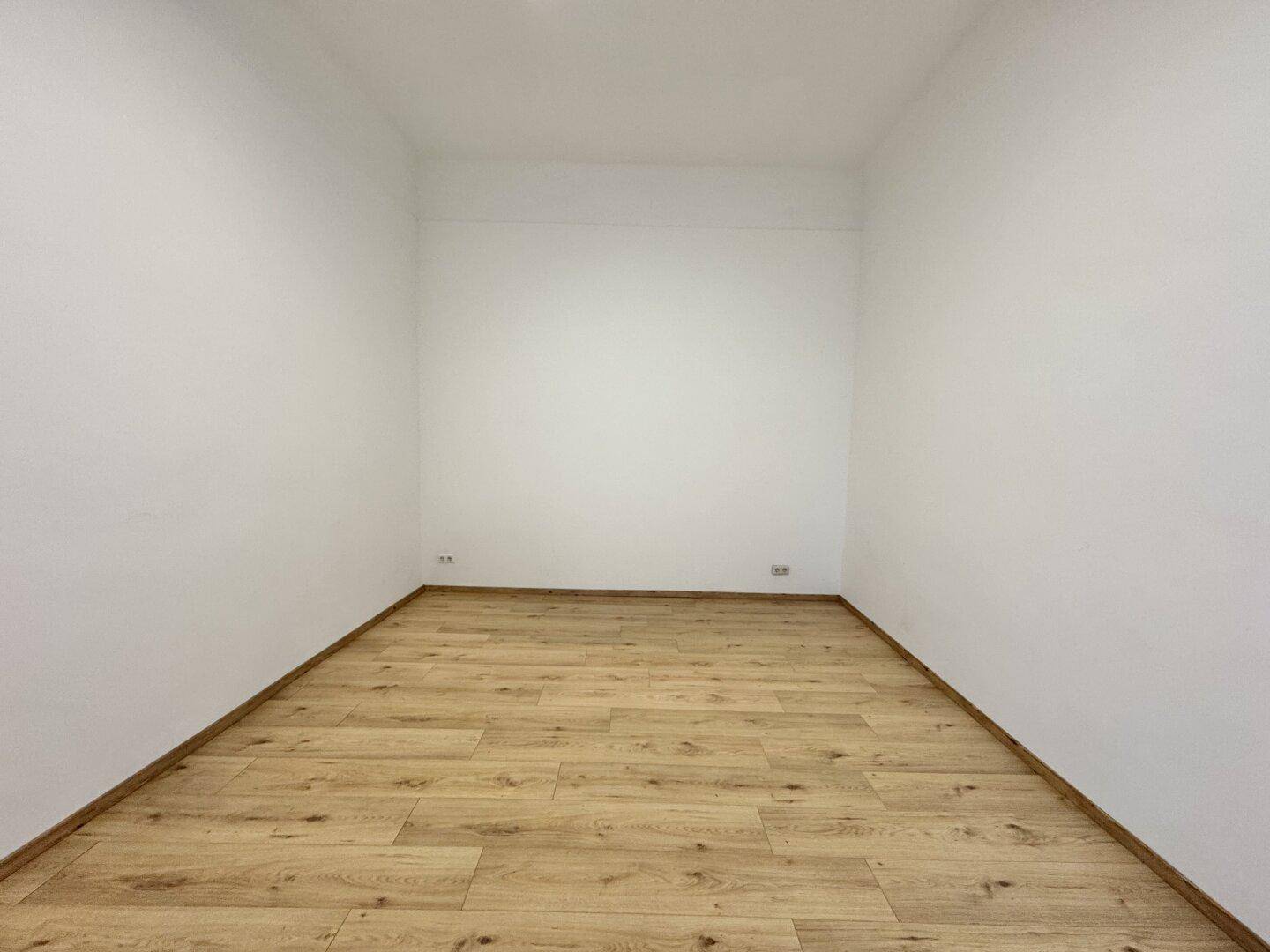 Schlichter, leerer Raum mit Holzboden und weißen Wänden, ideal für vielfältige Nutzung.