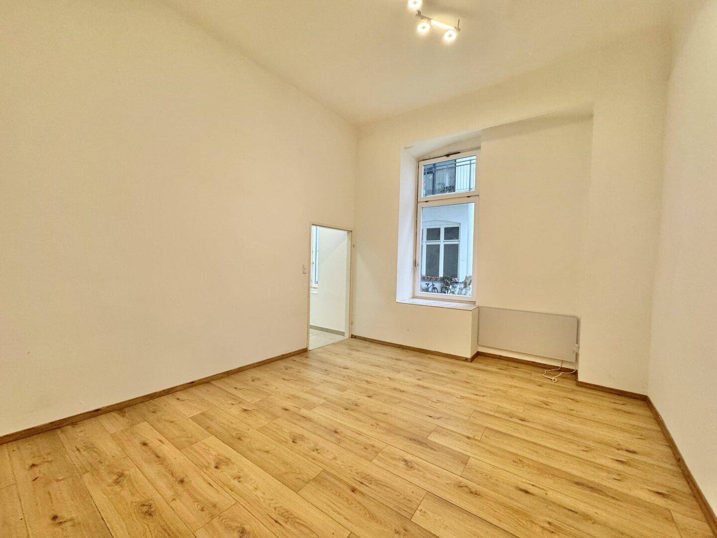 Leerer Raum mit Holzboden und Fenster zum Innenhof, bereit zur individuellen Gestaltung.