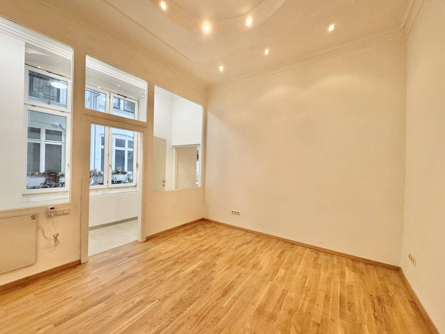 Geräumiges Wohnzimmer mit Parkettboden, hohen Decken und dekorativer Stuckverzierung.