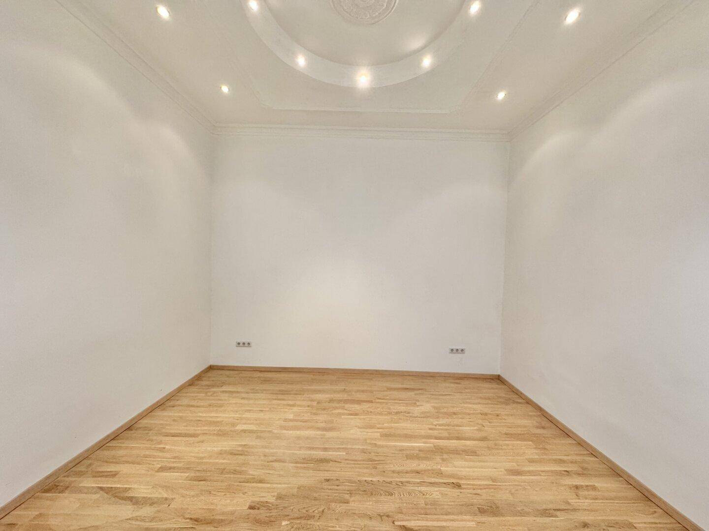 Leerer Raum mit Parkettboden und eleganter Stuckdecke, bereit zur Einrichtung.