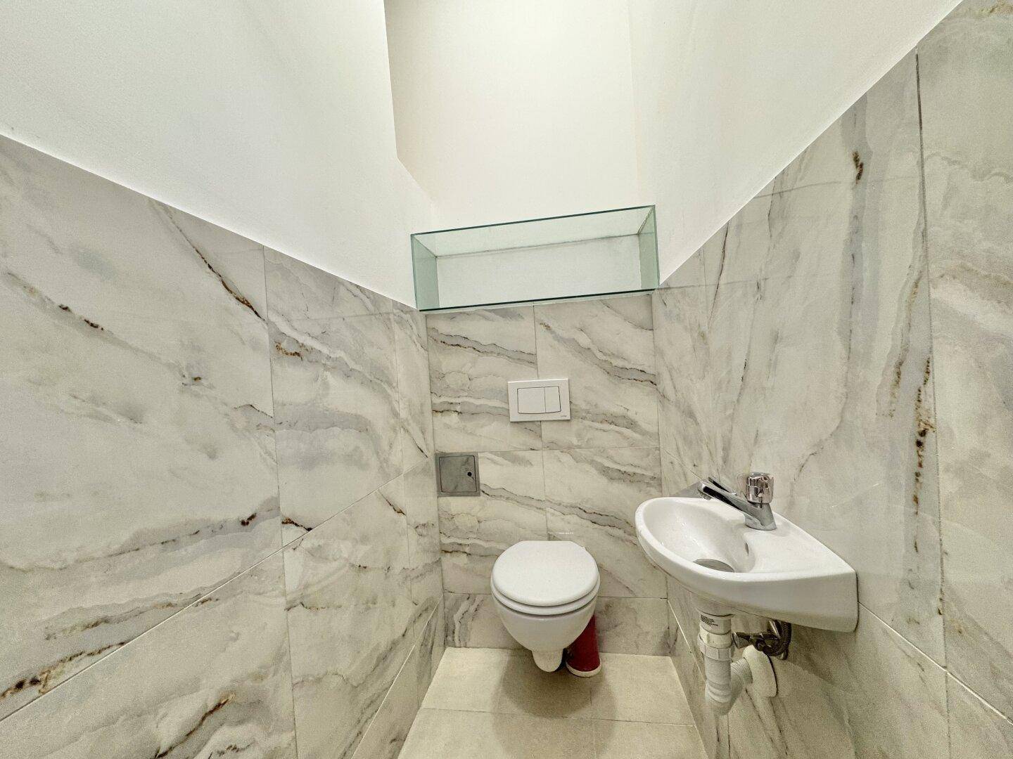 Separates WC mit modernen Marmorfliesen, wandhängender Toilette und kleinem Waschbecken.