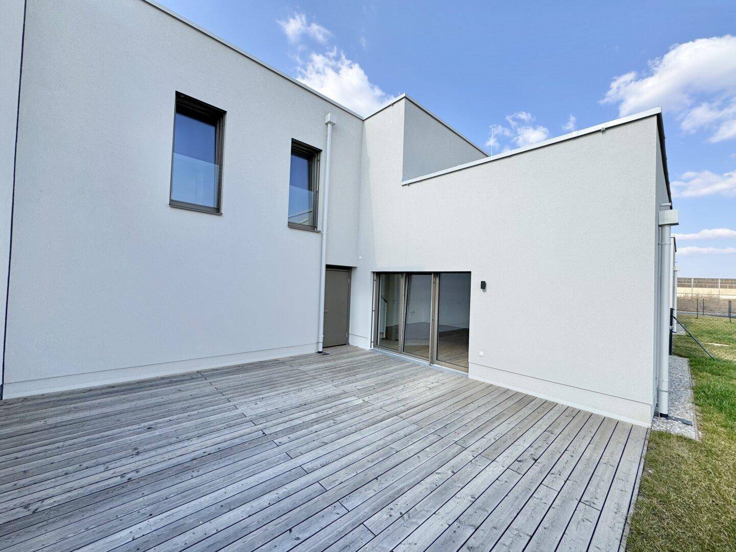 Großzügige Holzterrasse an der Rückseite des modernen Hauses, ideal für Entspannung im Freien.