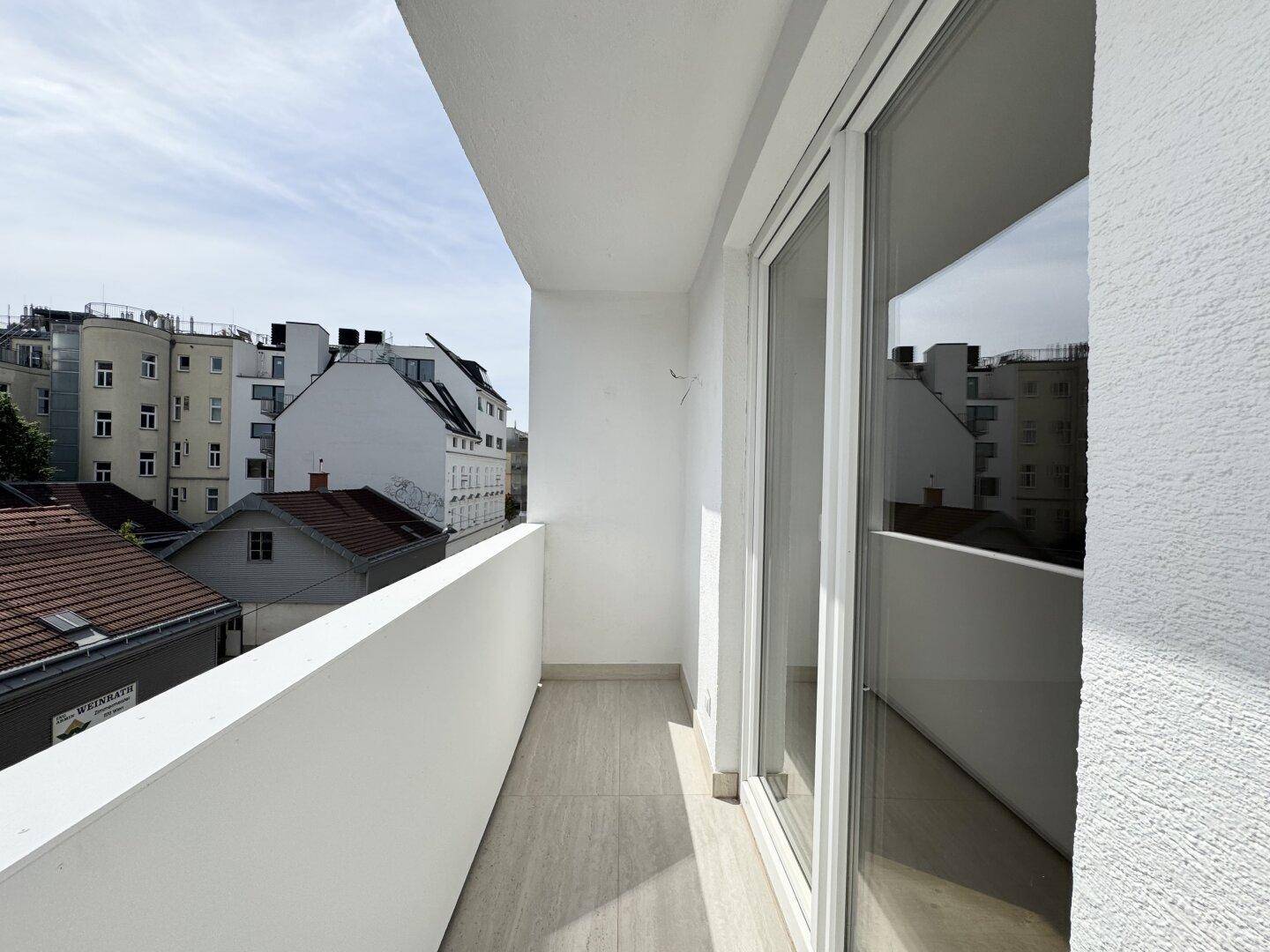 Schmaler Balkon mit Fliesenboden und Blick auf die umliegenden Gebäude der Stadt.