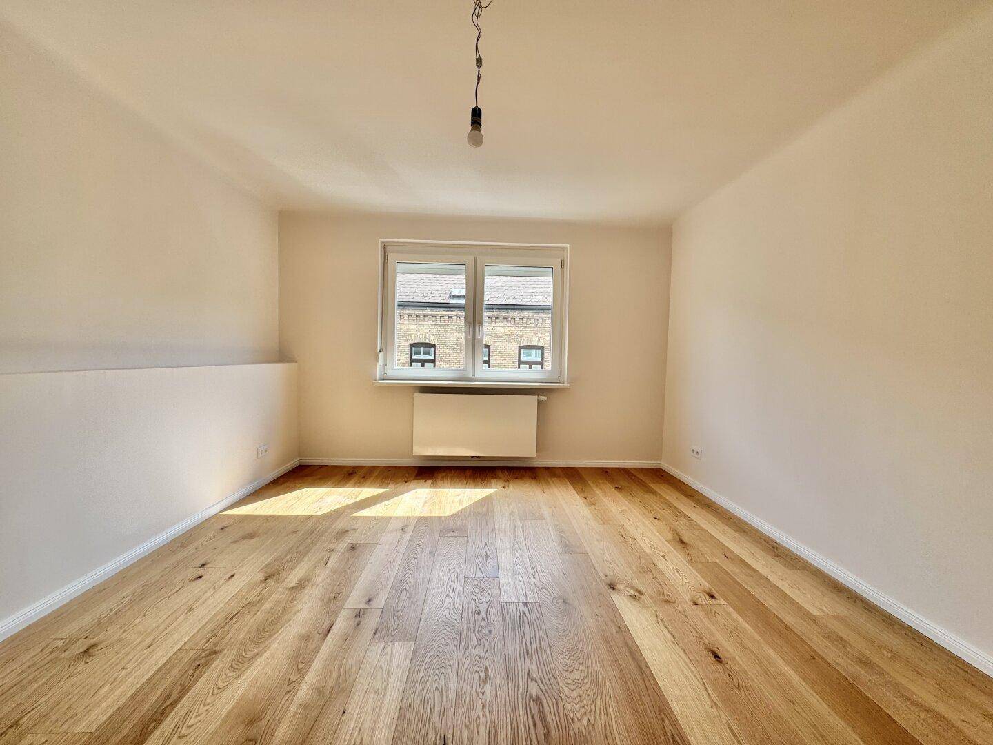 Leeres Schlafzimmer mit Holzboden, großem Fenster und viel natürlichem Licht.