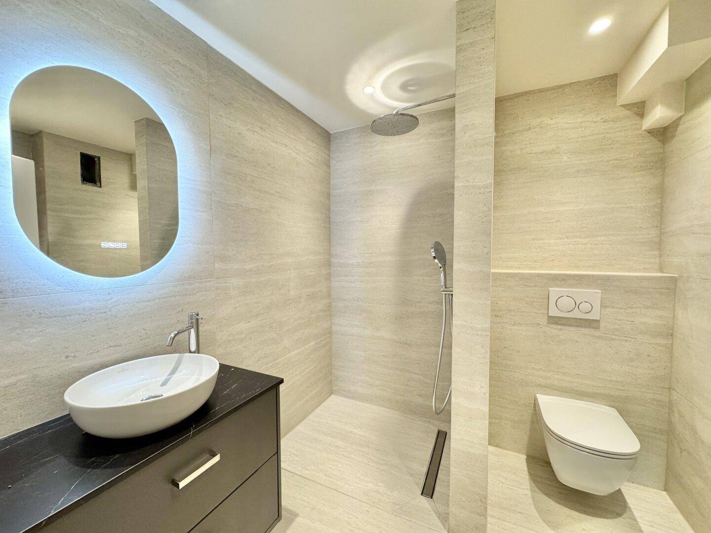 Modernes Badezimmer mit begehbarer Dusche, beleuchtetem Spiegel und Wand-WC.