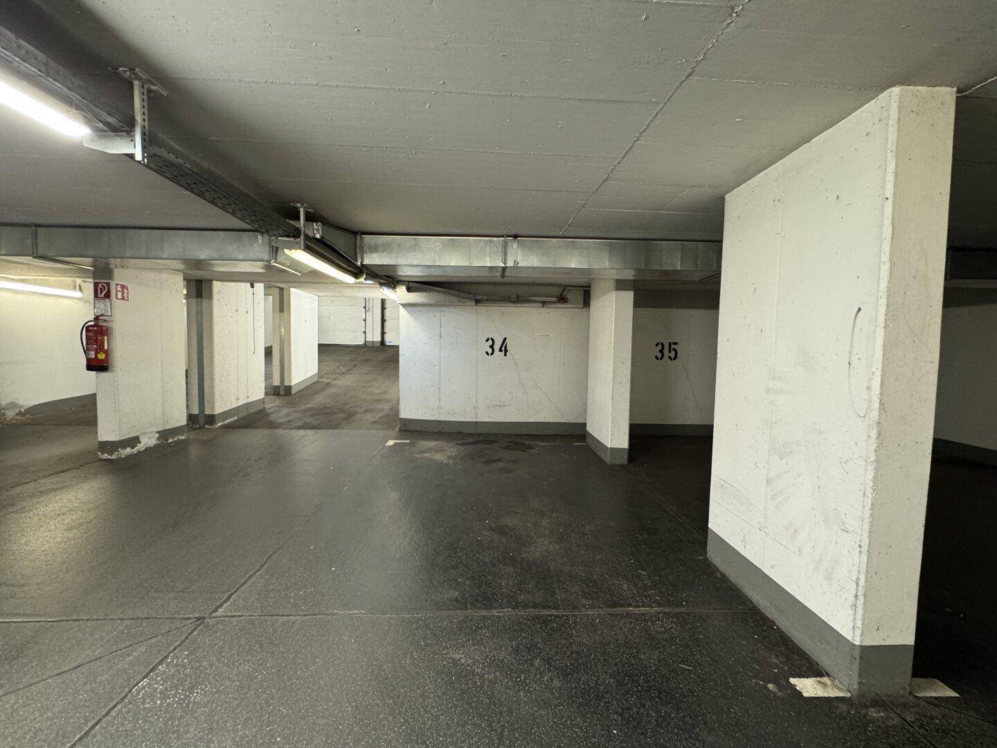 Saubere und gut beleuchtete Tiefgarage mit Betonpfeilern und einem Feuerlöscher an der Wand.
