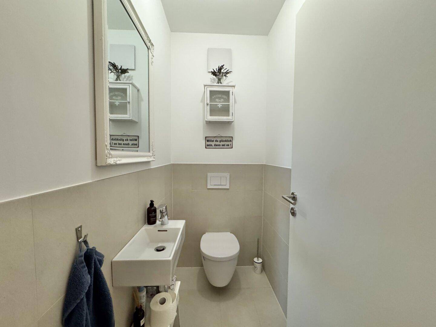 Modernes Gäste-WC mit Wand-WC, kleinem Waschbecken und Spiegel.