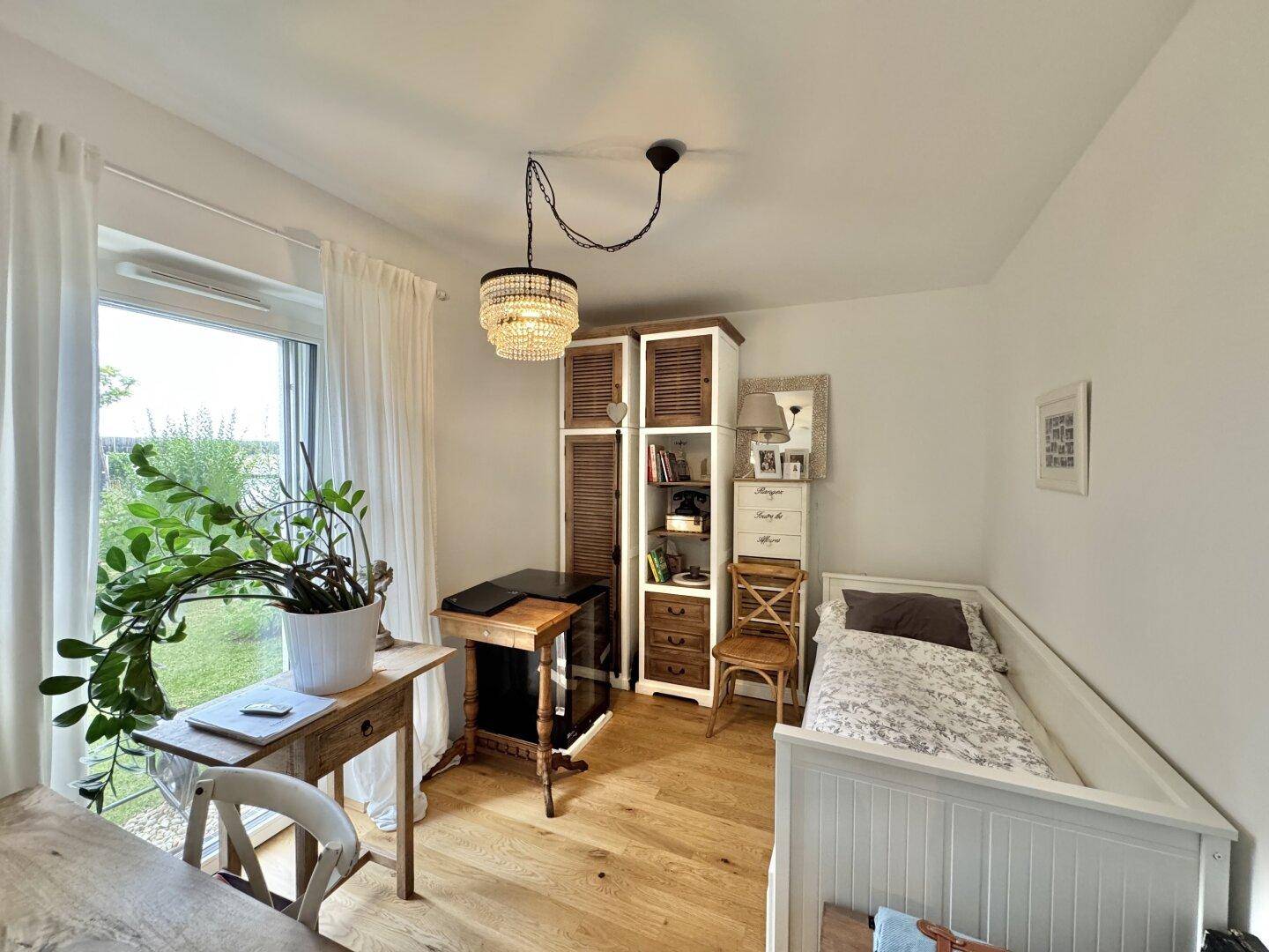 Helles Schlafzimmer mit Einzelbett, Schreibtisch und Blick ins Grüne.