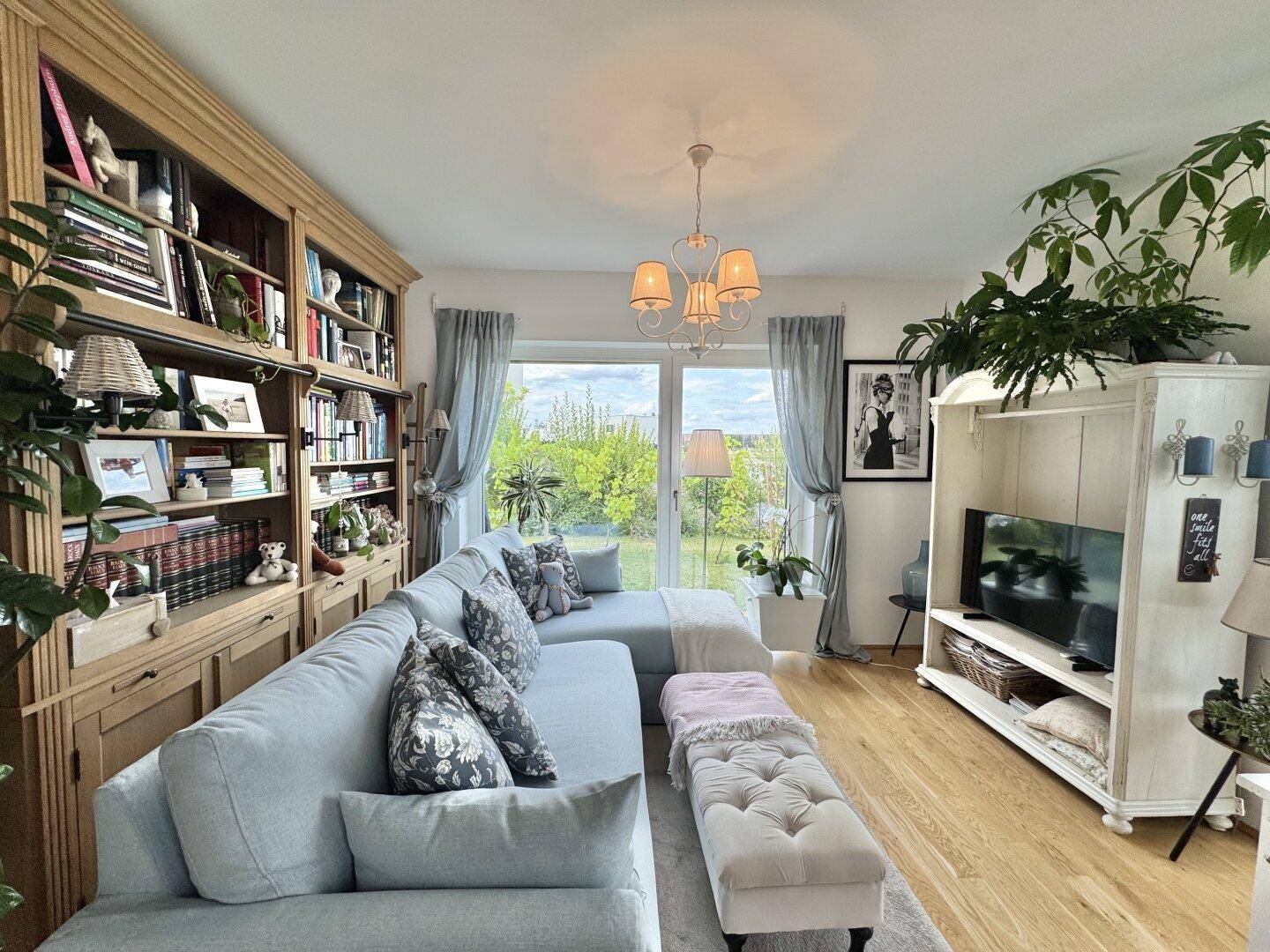 Gemütliches Wohnzimmer mit großem Sofa, Bücherregal und Blick in den grünen Garten.