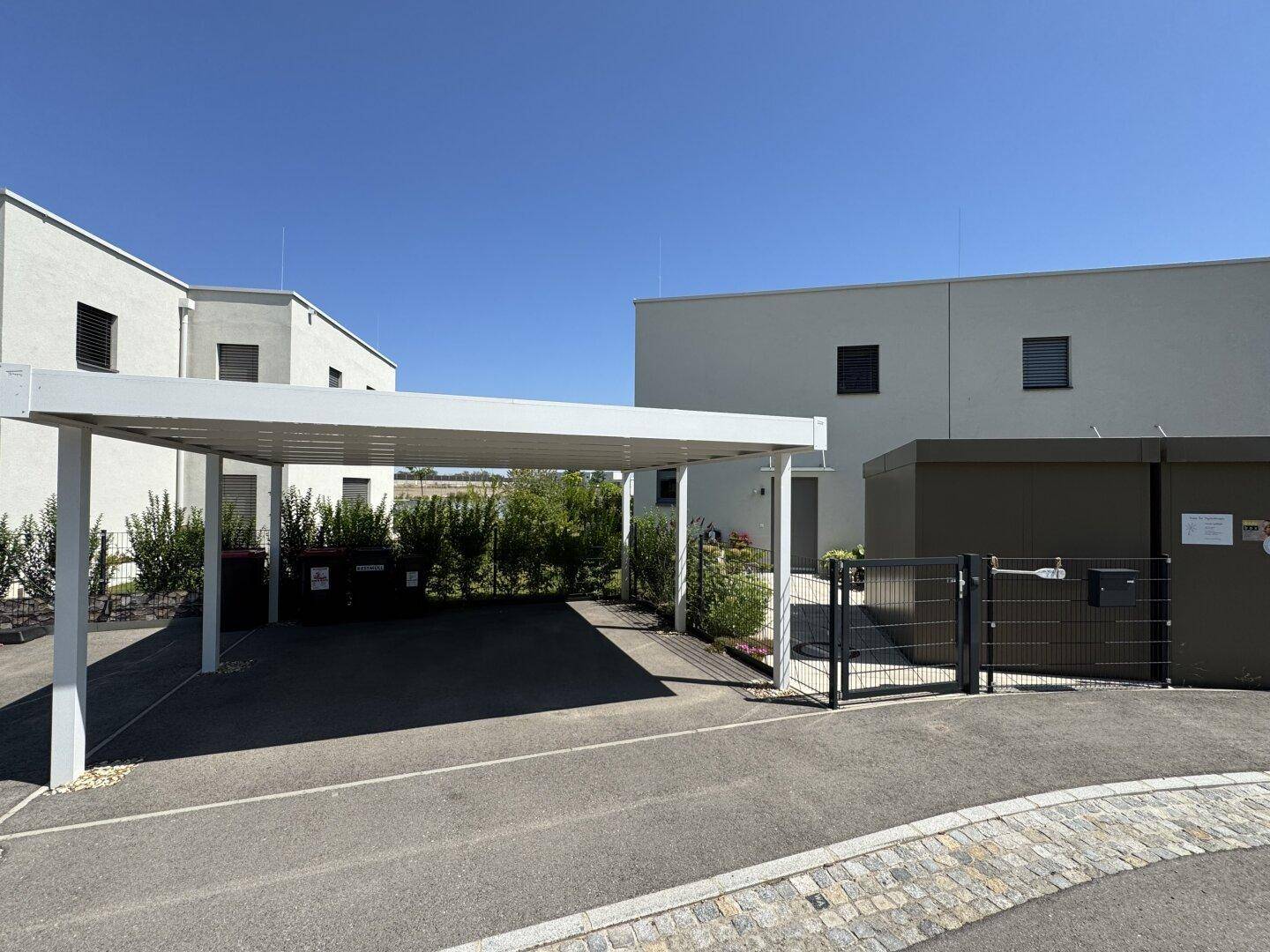 Moderner Carport und Eingangstor zu den Wohnhäusern in einer sonnigen Wohnsiedlung.