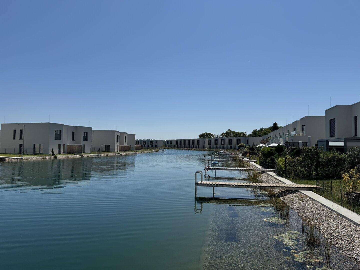 Weitläufiger See mit Reihen moderner Häuser und privaten Stegen unter klarem blauem Himmel.