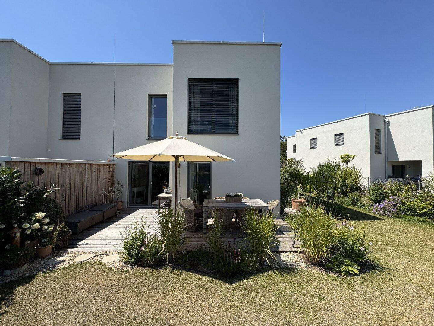 Moderner Gartenbereich mit Holzterrasse, Sitzgelegenheiten und gepflegtem Rasen hinter dem Haus.