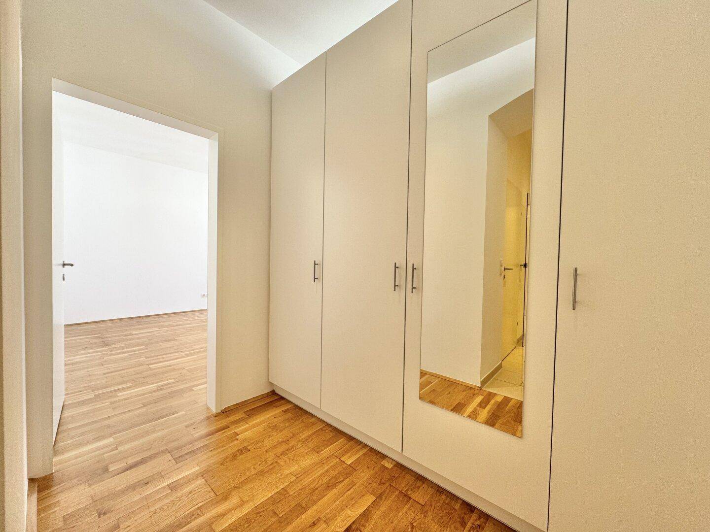 Heller Flur mit Einbauschränken und Spiegel, bietet praktischen Stauraum und Zugang zu weiteren Räumen.