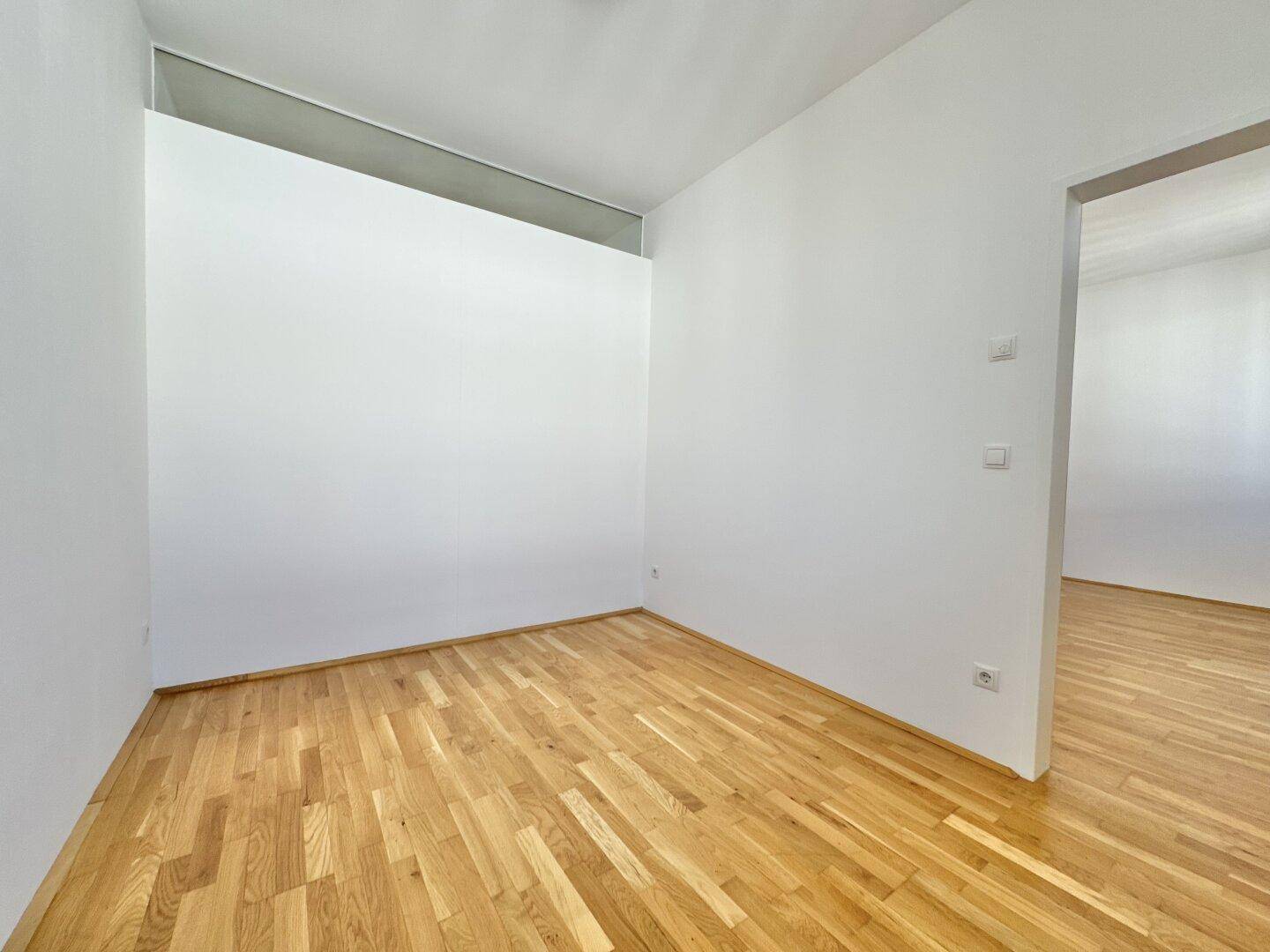 Kleinerer, heller Raum mit Parkettboden und weiß gestrichenen Wänden, ideal für ein Büro oder Gästezimmer.