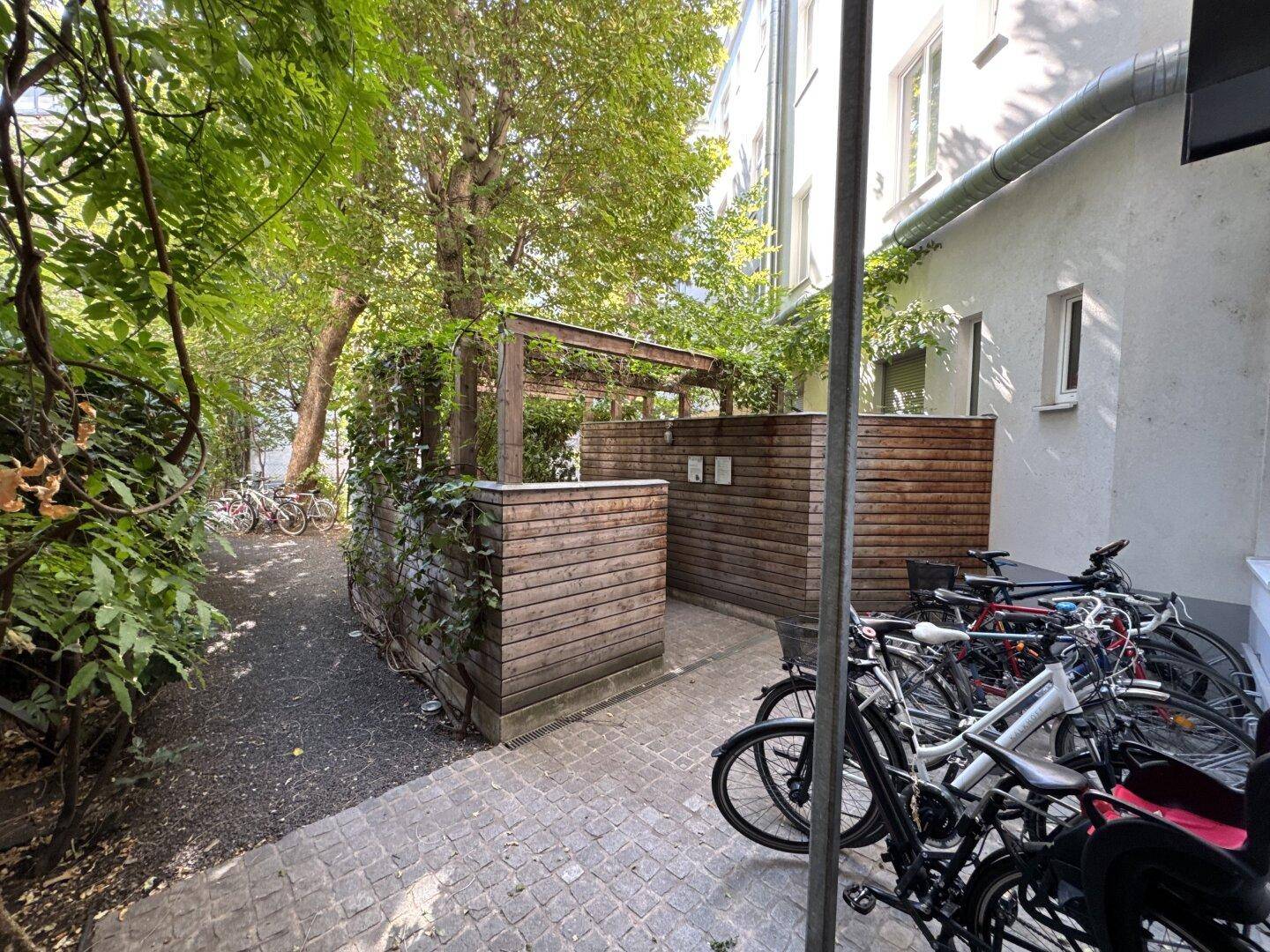 Gemeinschaftlicher Gartenbereich mit Fahrradabstellplätzen und viel Grün, umgeben von Bäumen.