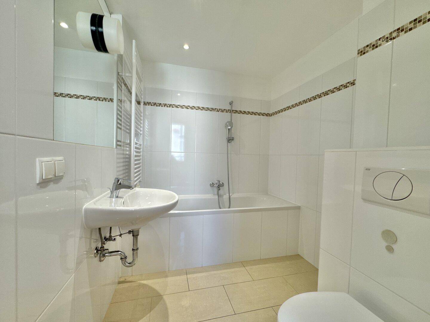 Modernes Badezimmer mit weißen Fliesen, Badewanne mit Duschfunktion und beheiztem Handtuchhalter.