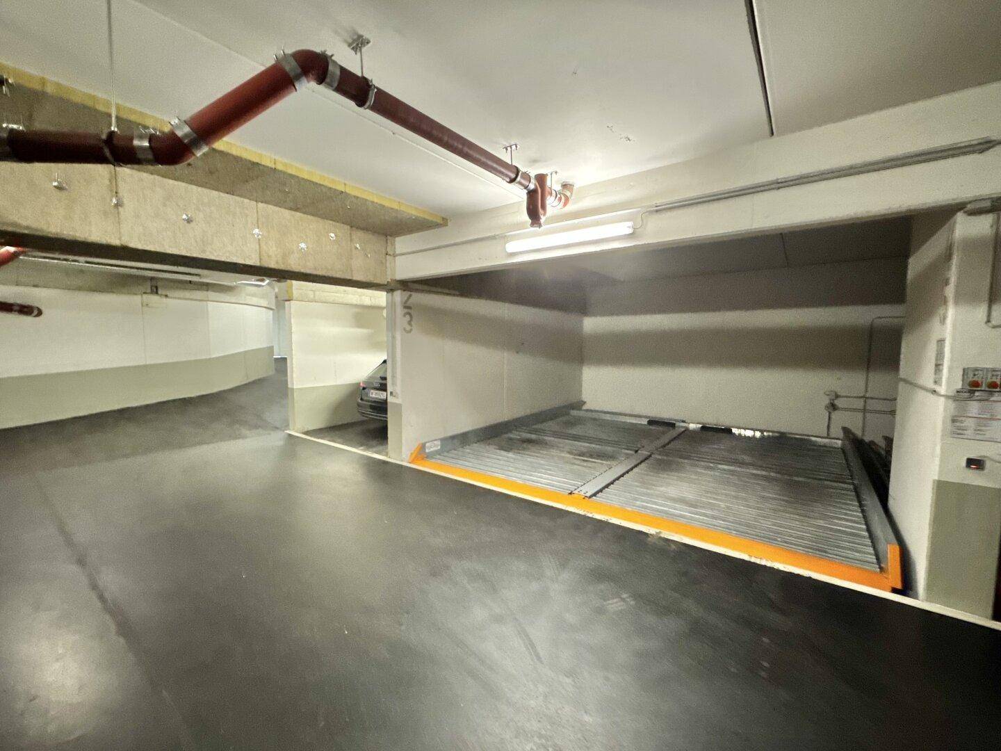 Blick in eine Tiefgarage mit mechanischem Parksystem und sichtbaren Versorgungsleitungen an der Decke.