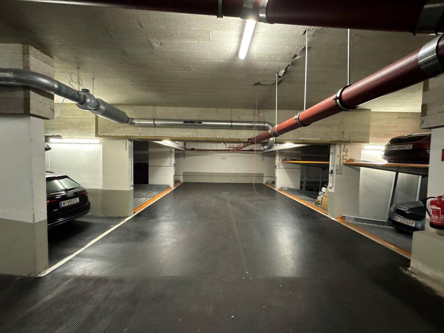 Geräumige Tiefgarage mit mehreren Stellplätzen, sichtbaren Rohren und einfacher Beleuchtung.