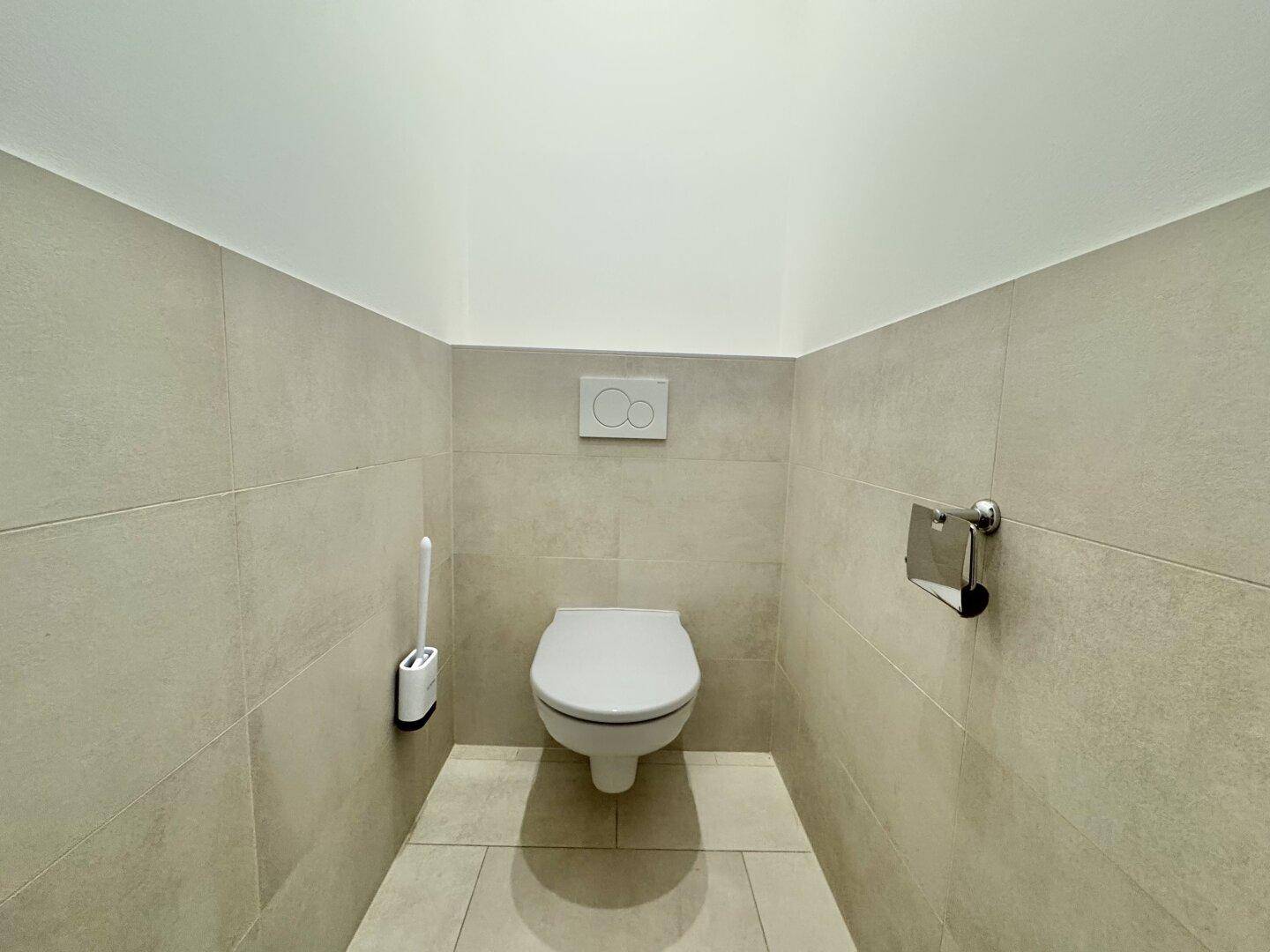 Separates WC mit Wand-WC und hellen Fliesen an Wänden und Boden.