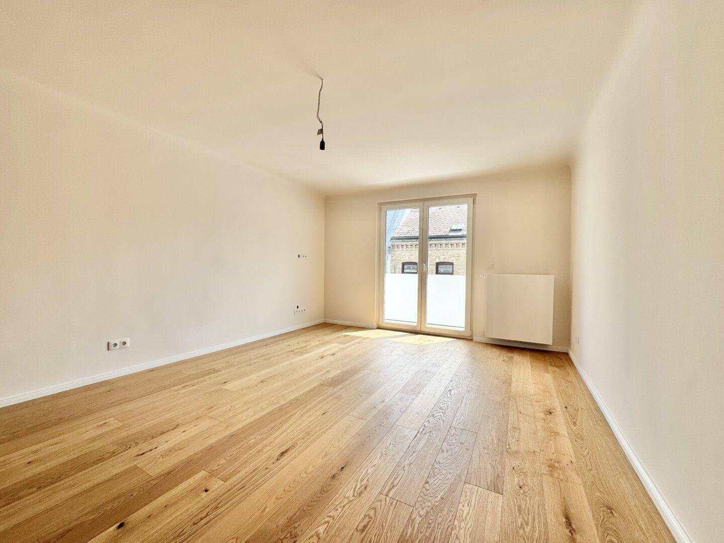 Heller, leerer Raum mit Holzboden und großem Fenster, ideal für individuelle Gestaltung.
