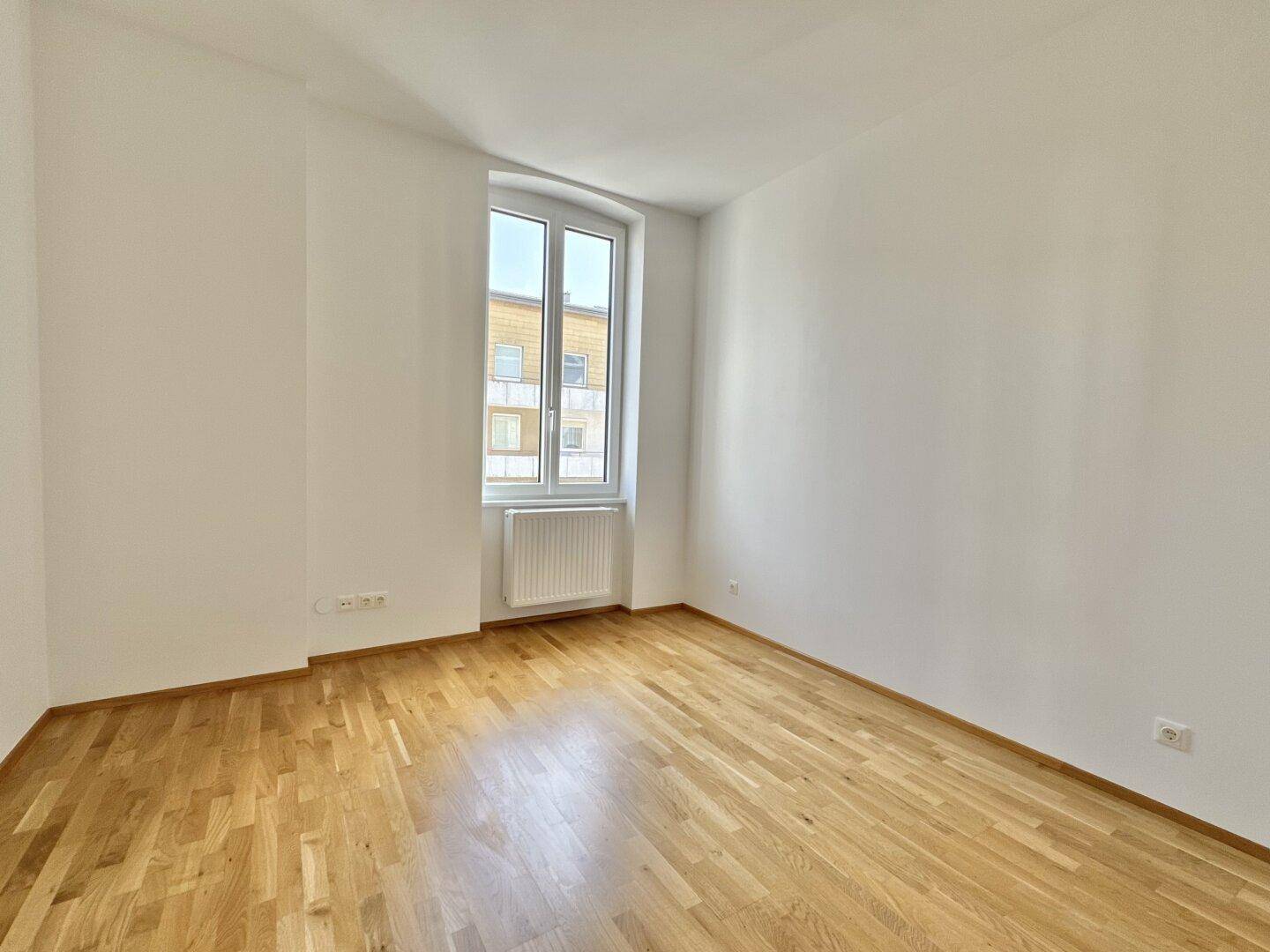 Helles Schlafzimmer mit Parkettboden und einem großen Fenster.