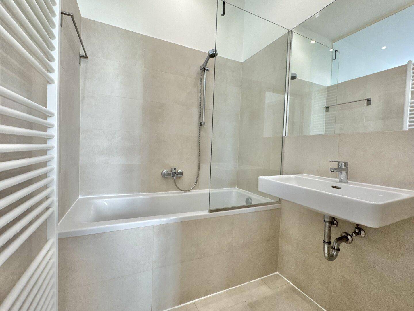 Modernes Badezimmer mit Badewanne, Duschabtrennung und beheiztem Handtuchhalter.