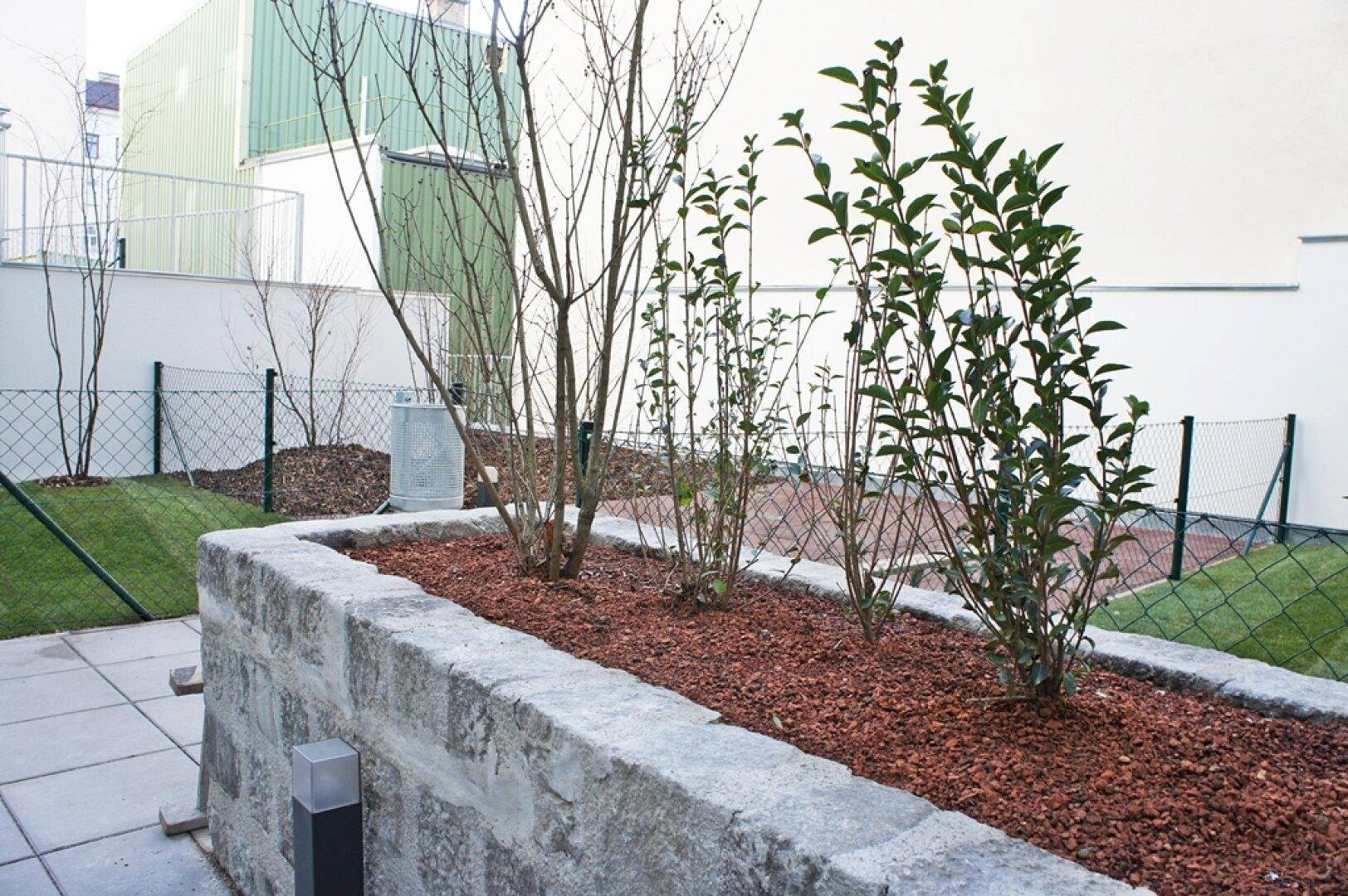 Gepflegter Gartenbereich mit Hochbeet und jungen Pflanzen, umzäunt.
