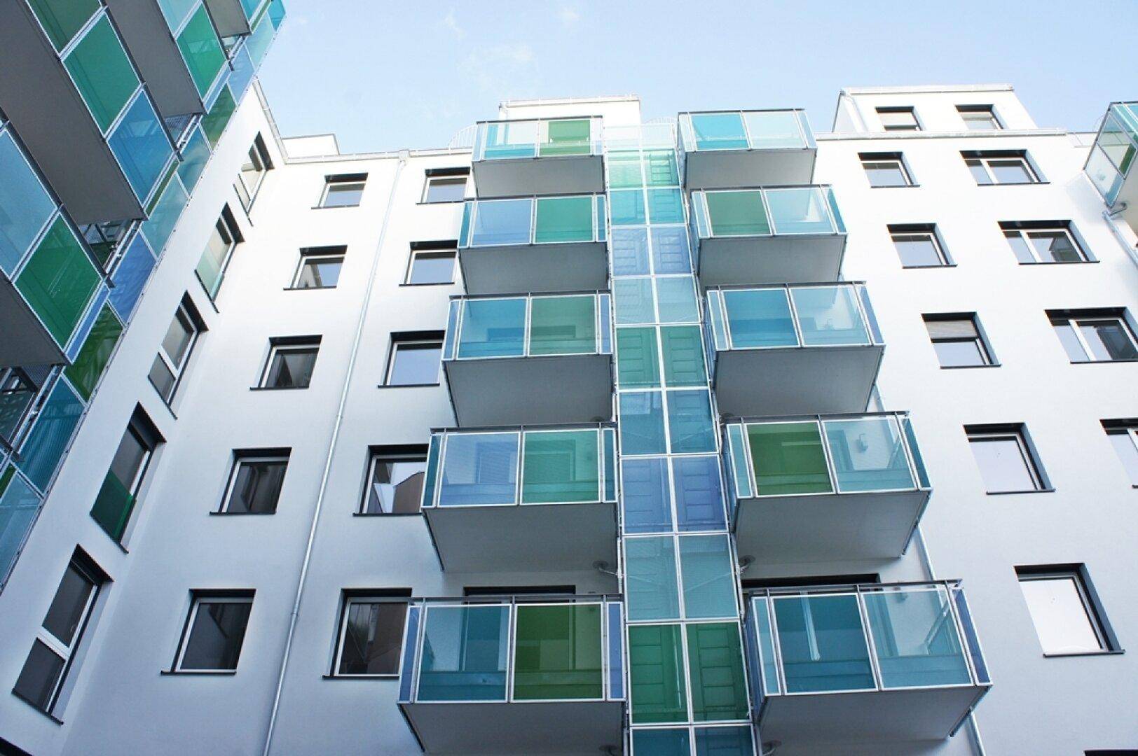 Moderne Wohnhausfassade mit farbigen Balkonverkleidungen und vielen Fenstern.