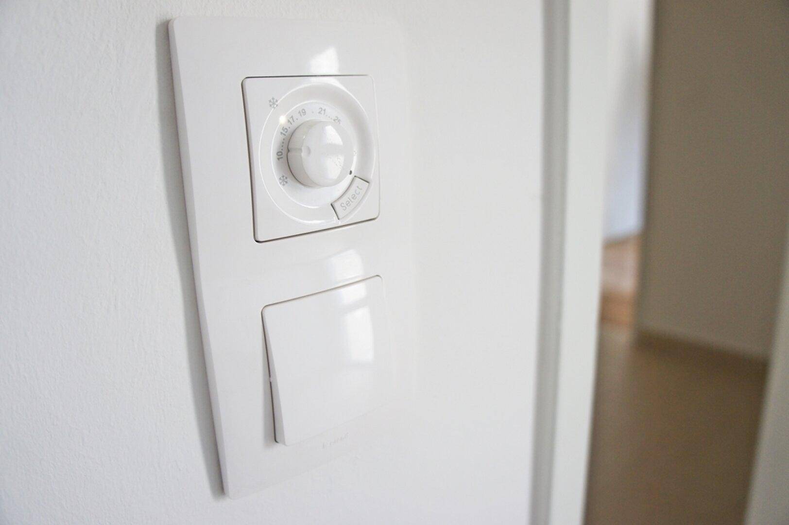 Detailaufnahme eines modernen Raumthermostats an einer weißen Wand.