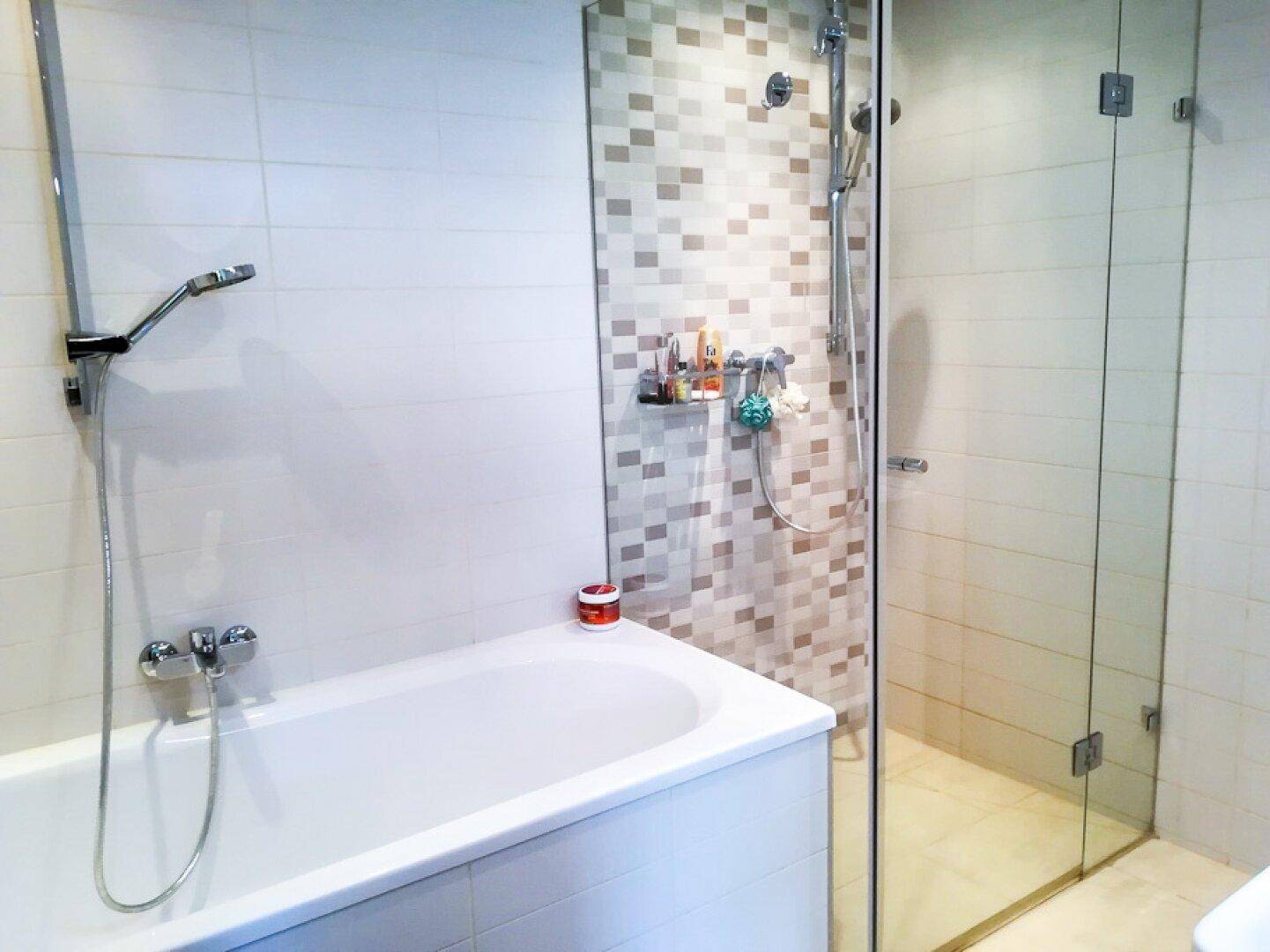 Badezimmer mit Badewanne und separater Duschkabine, gefliest in hellen Farbtönen.