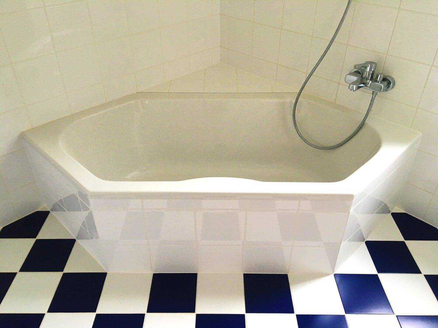 Badezimmer mit Eckbadewanne und auffälligen blau-weißen Schachbrettfliesen am Boden.