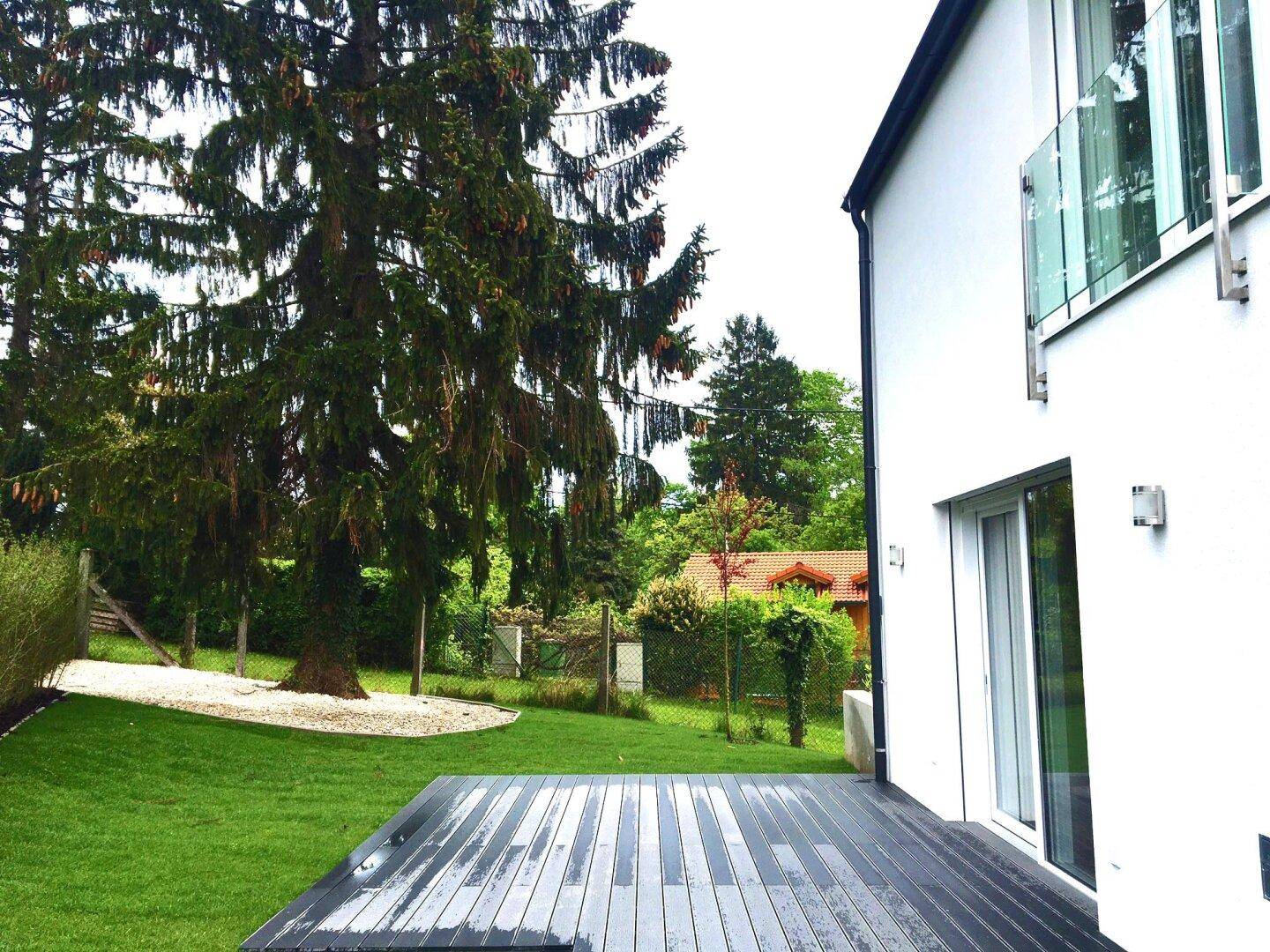 Moderne Holzterrasse im Gartenbereich, umgeben von Bäumen und Grünflächen.