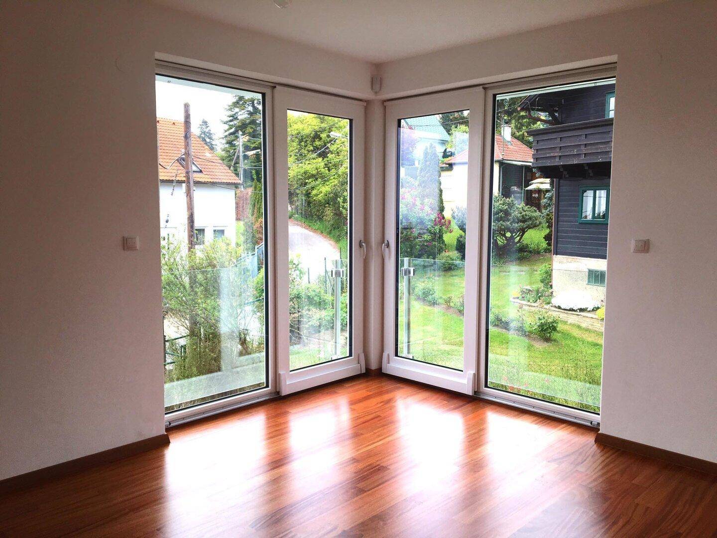 Heller Eckraum mit großen Fenstern, die einen Blick ins Grüne und auf die Umgebung bieten.