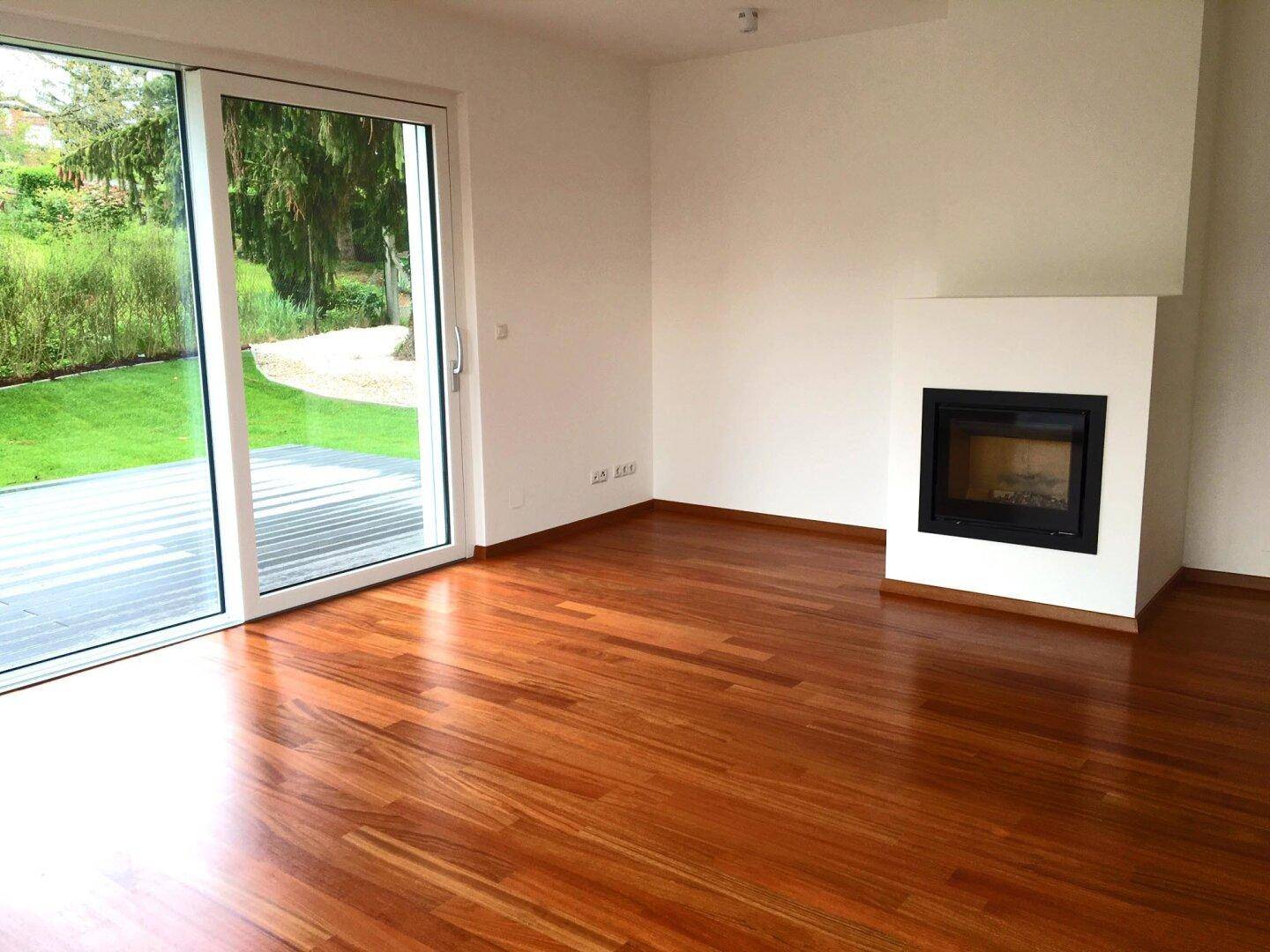 Helles Wohnzimmer mit Parkettboden, integriertem Kamin und großem Fenster zum Garten.