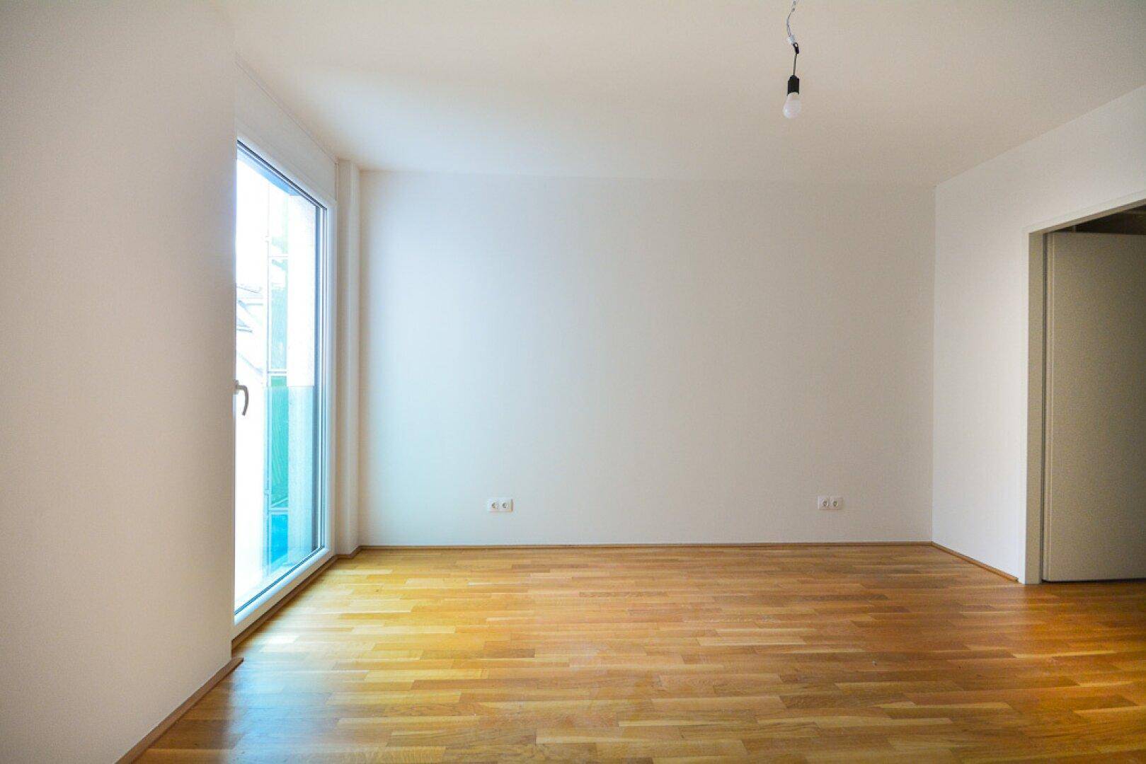 Heller Raum mit Parkettboden und großem Fenster, ideal als Wohn- oder Schlafzimmer.