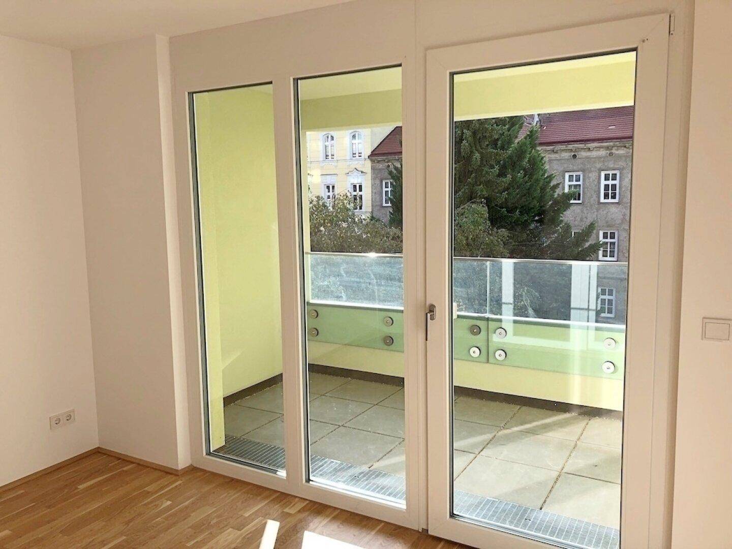 Heller Raum mit großen Fenstertüren, die auf den Balkon führen und viel Tageslicht hereinlassen.