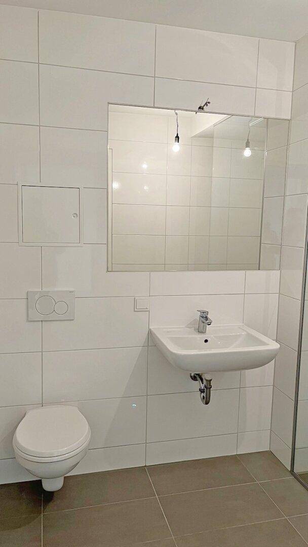 Modernes Badezimmer mit weißen Fliesen, wandhängendem WC und Waschbecken.