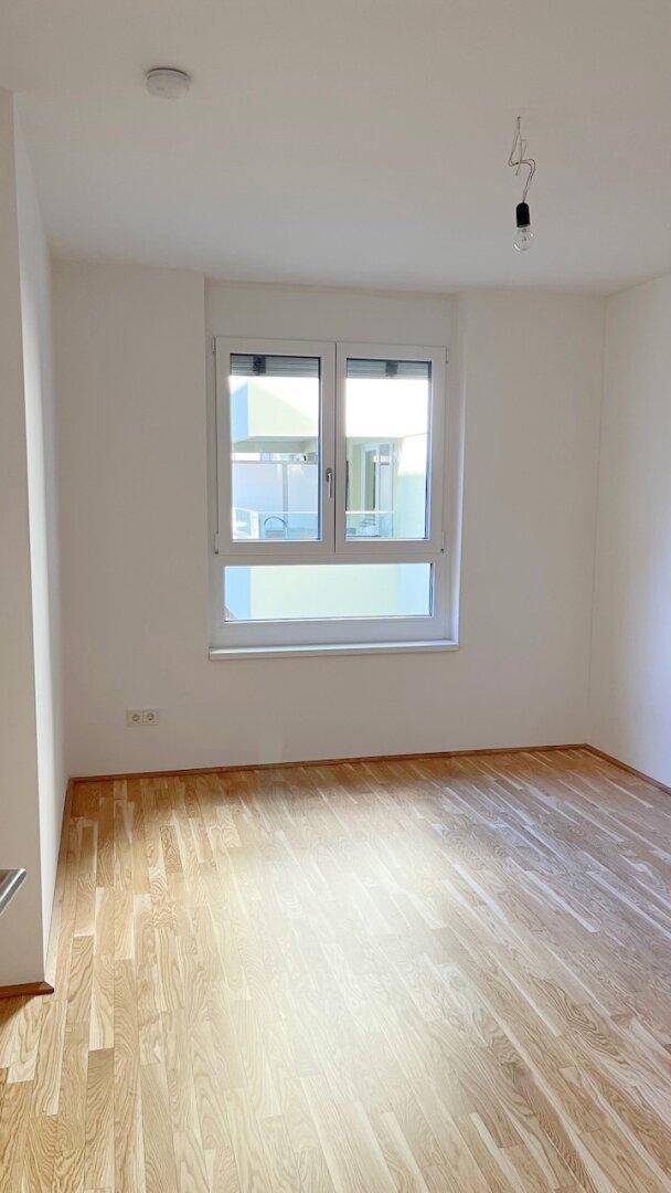 Helles Schlafzimmer mit Parkettboden und einem Fenster, das viel natürliches Licht spendet.