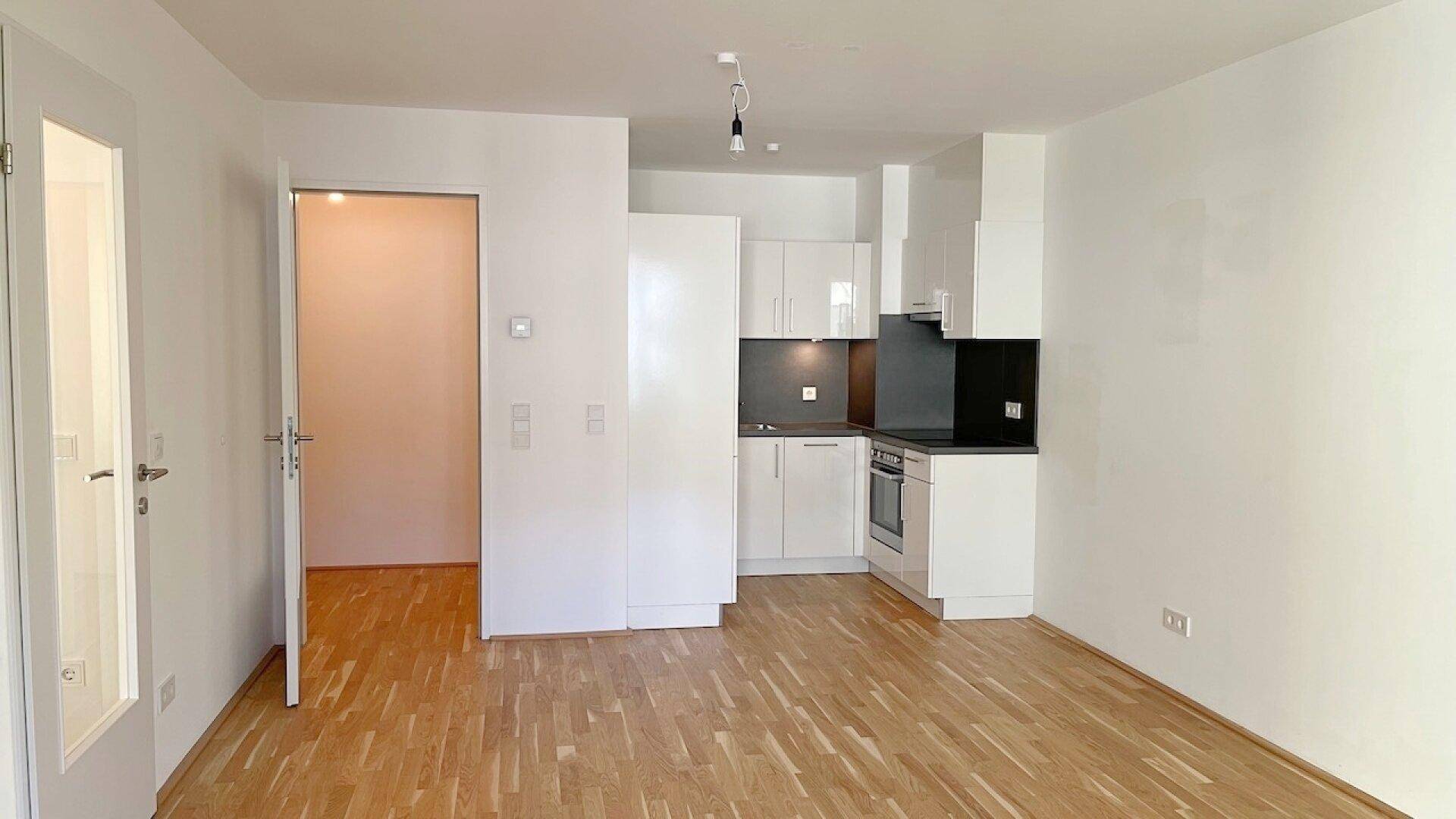Offener Wohnbereich mit heller Einbauküche und Parkettboden, ideal für modernes Wohnen.