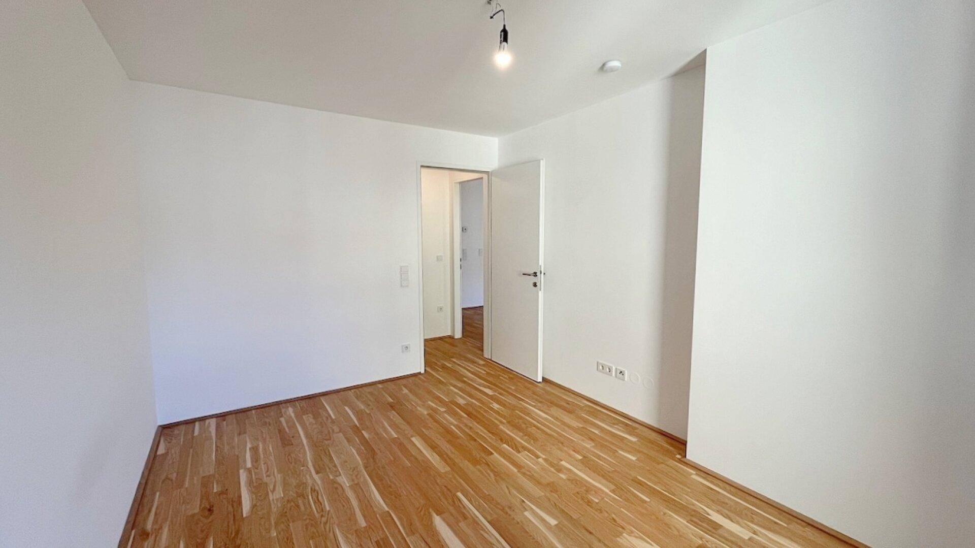 Leeres Zimmer mit hellem Parkettboden und weißen Wänden, bereit zur individuellen Gestaltung.
