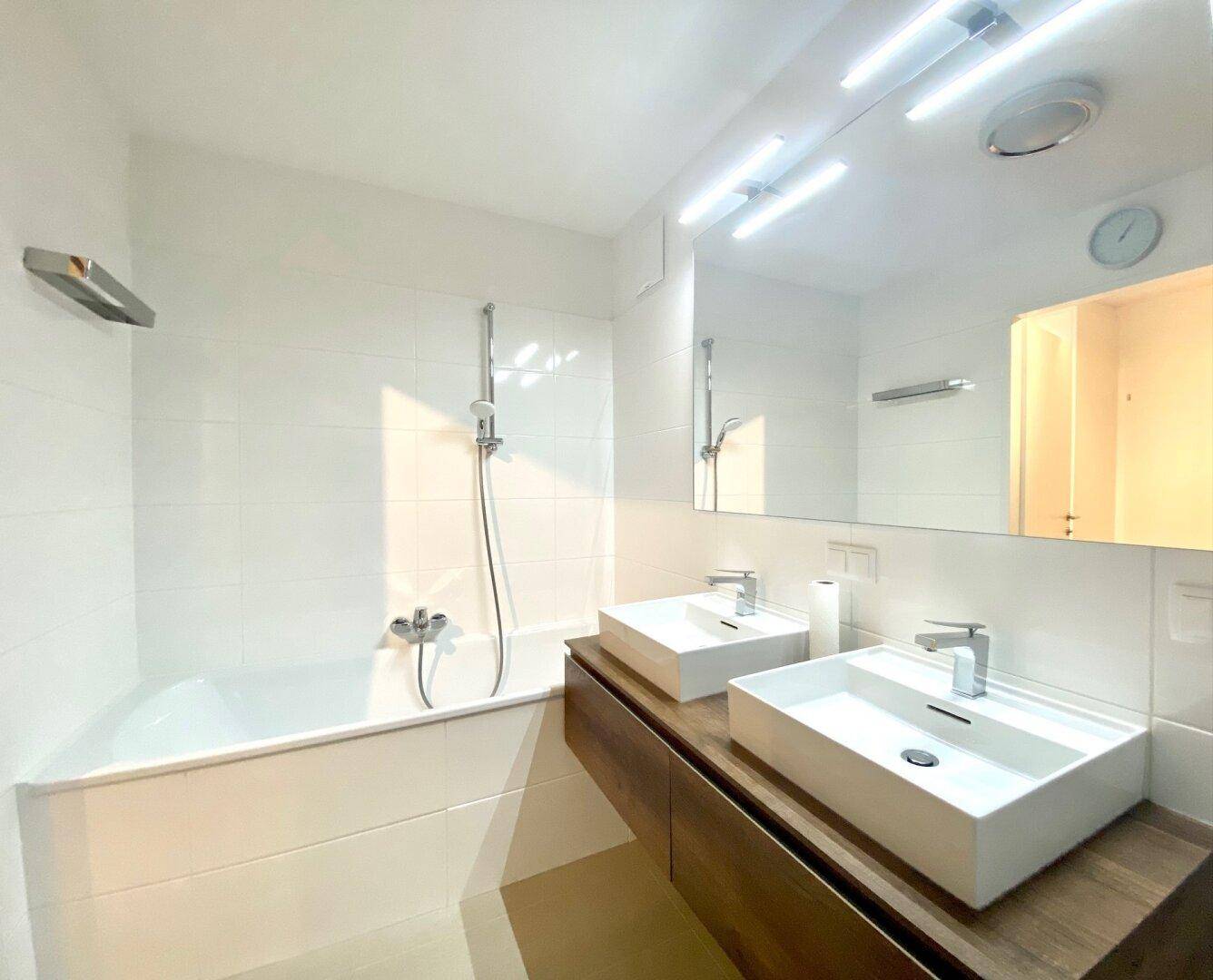 Modernes Badezimmer mit Doppelwaschbecken, Badewanne und weißen Fliesen.