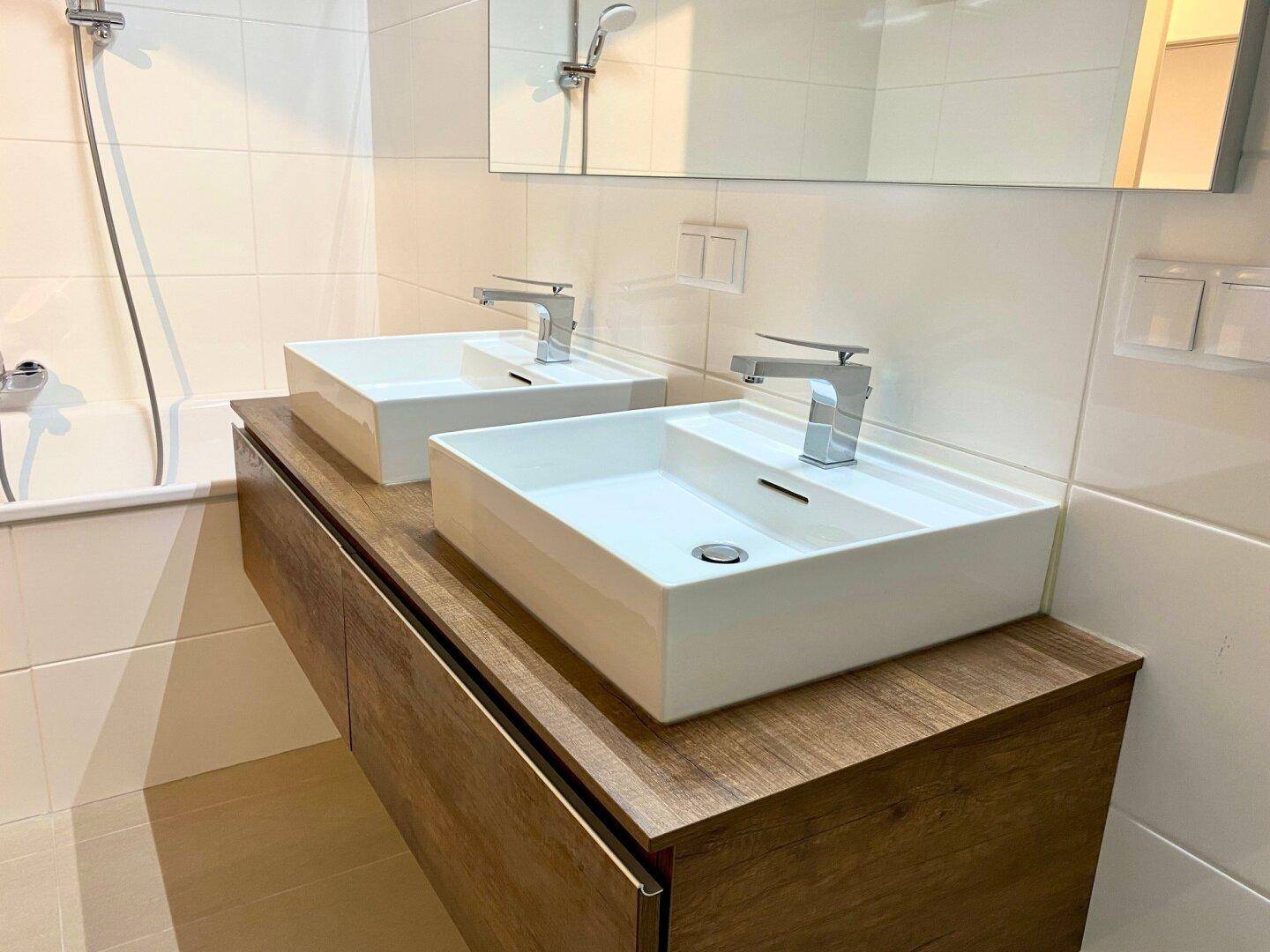 Badezimmer mit zwei Aufsatzwaschbecken auf Holzunterschrank und weißen Wandfliesen.