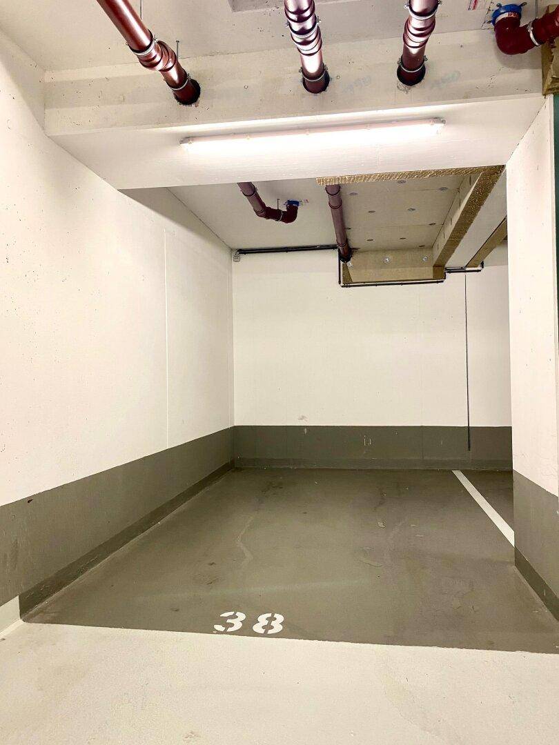 Tiefgaragenstellplatz Nummer 38 mit Betonboden und sichtbaren Leitungen an der Decke des Kellers.