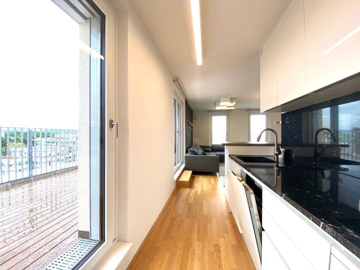 Helle Küche mit Zugang zum Balkon, schwarzen Arbeitsplatten und modernen Geräten.