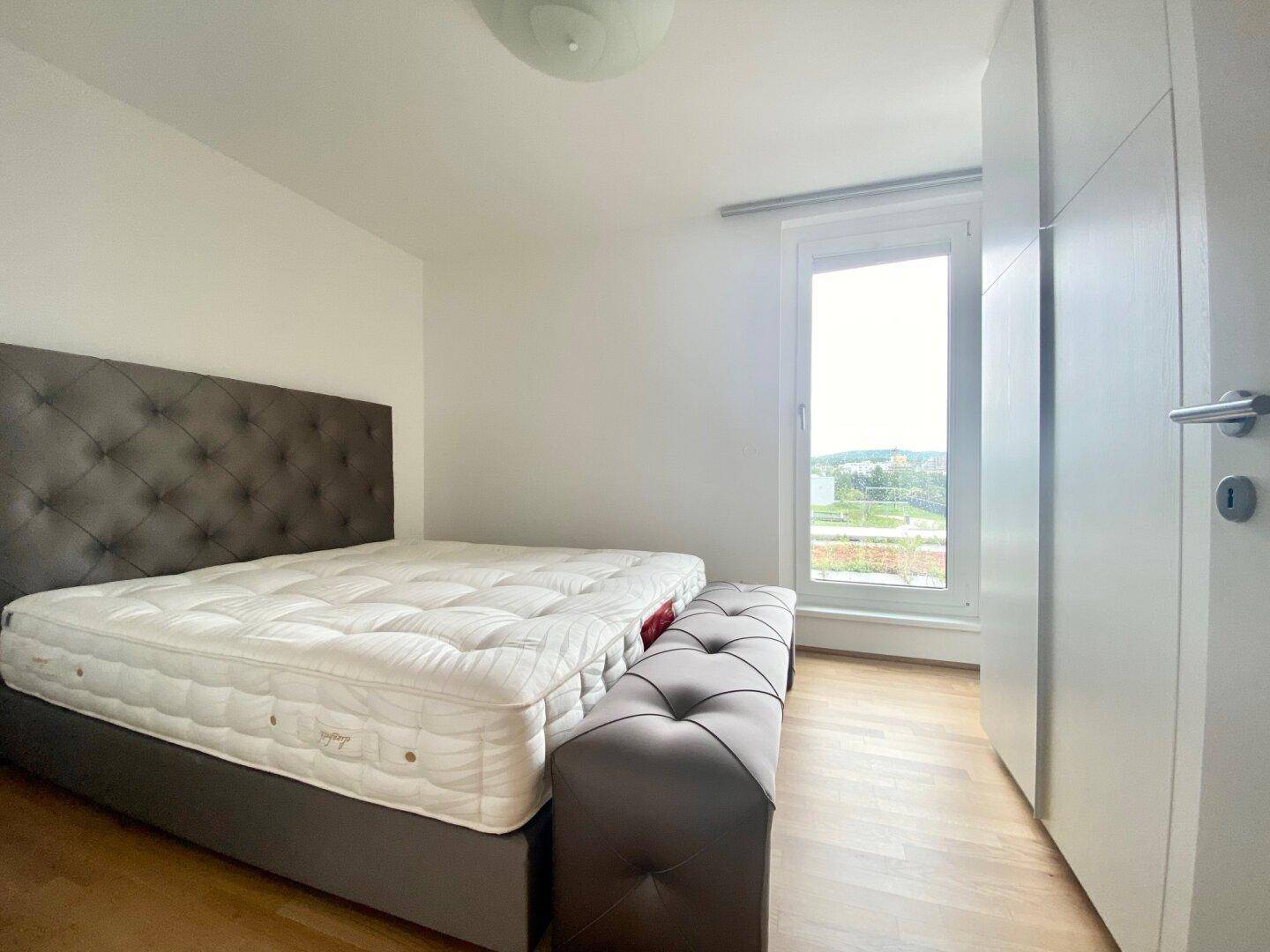Schlafzimmer mit Doppelbett, Holzboden und großem Fenster mit Ausblick.
