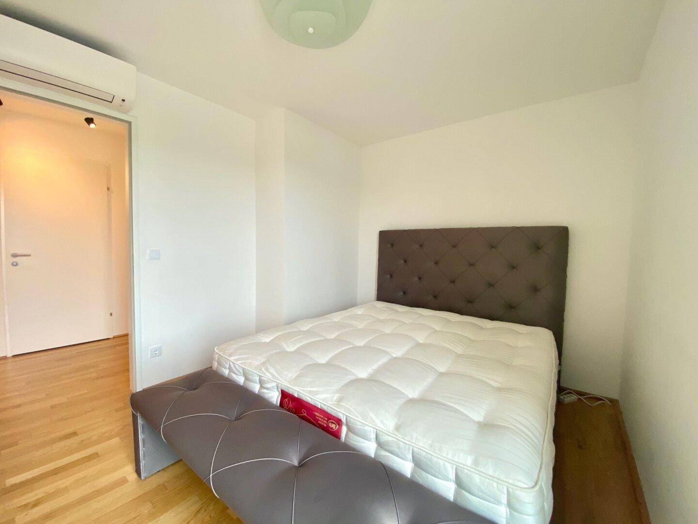 Helles Schlafzimmer mit Doppelbett, Holzboden und Blick nach draußen.