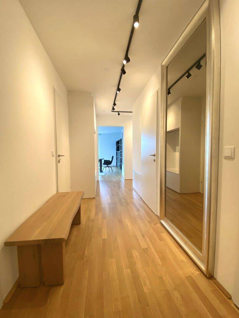Heller Flur mit Holzboden, großem Spiegel und moderner Deckenbeleuchtung.