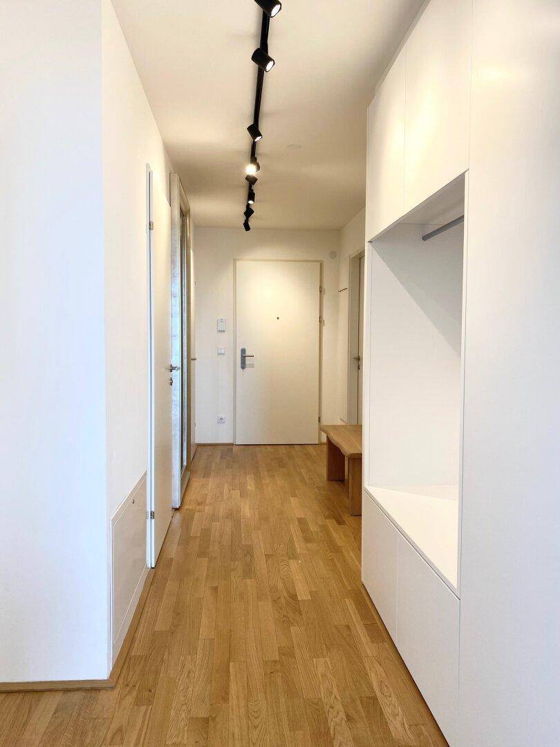Langer, heller Flur mit Holzboden, Einbauschränken und moderner Beleuchtung.